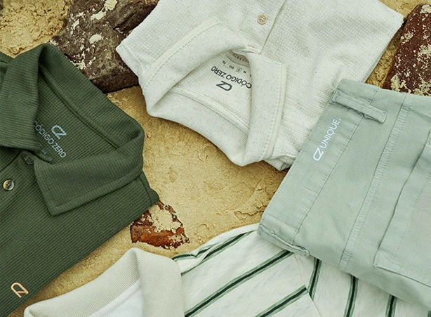 Sobre uma areia de praia e algumas rochas estão posicionadas formando um círculo 3 camisas polo Código Zero e uma outra peça que aparenta ser uma Calça Código Zero. A Polo de cima é branca com botões e possui uma textura natural, a polo à esquerda é verde, possui a logo CZ bordada na cor bege e uma textura diferenciada. A polo que se localiza na parte de baixo é listrada na cor verde. A calça à direita é na cor cinza esverdeado, bem neutra com a logo Unique bordada no cós na cor branca. #polomasculina #poloveraomasculino #polo #modamasculina #roupasparaoverao #polotexturizada #unique